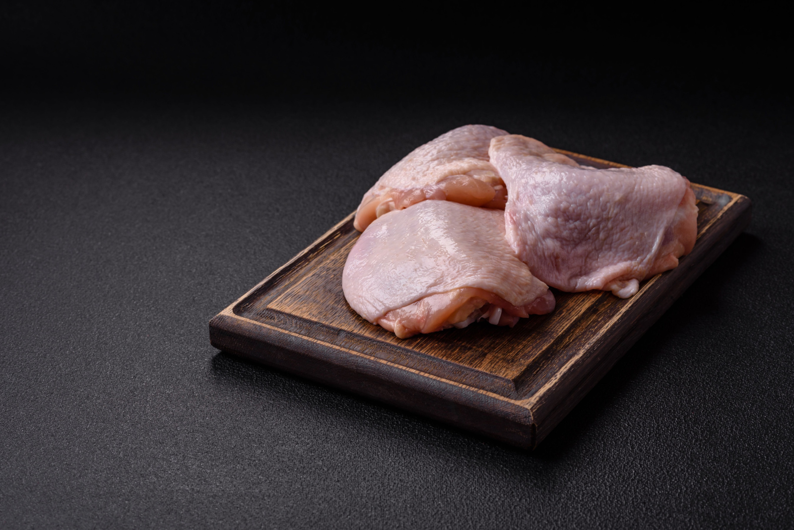Fresh raw chicken thighs with salt and spices on dark concrete background
