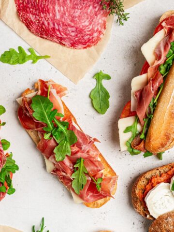 Assorted delicious baguette sandwiches filled with thinly sliced ham or salami and fresh green lettuce or arugula for breakfast arranged on white background, top view with copy space