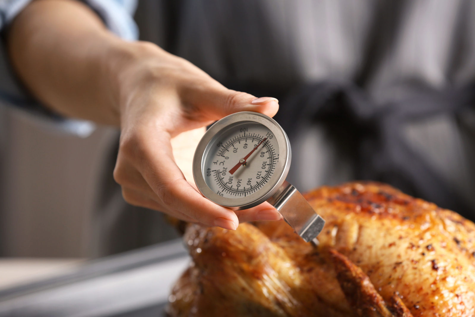Young woman measuring temperature of whole roasted turkey with meat thermometer