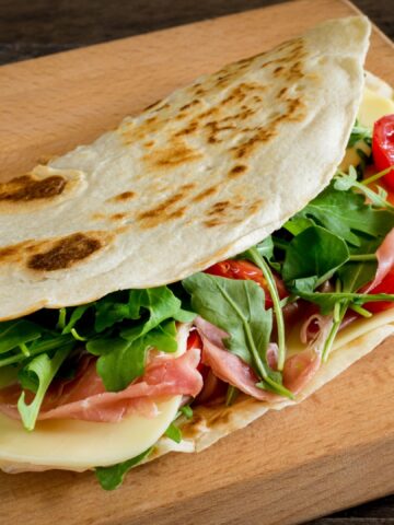 Romagna piadina filled with cheese,ham,tometoes and rocket on chopping board