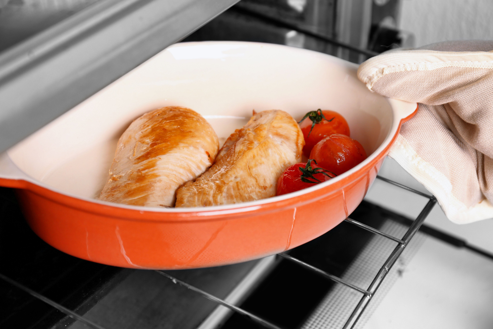 Human hand checking chicken breast in oven