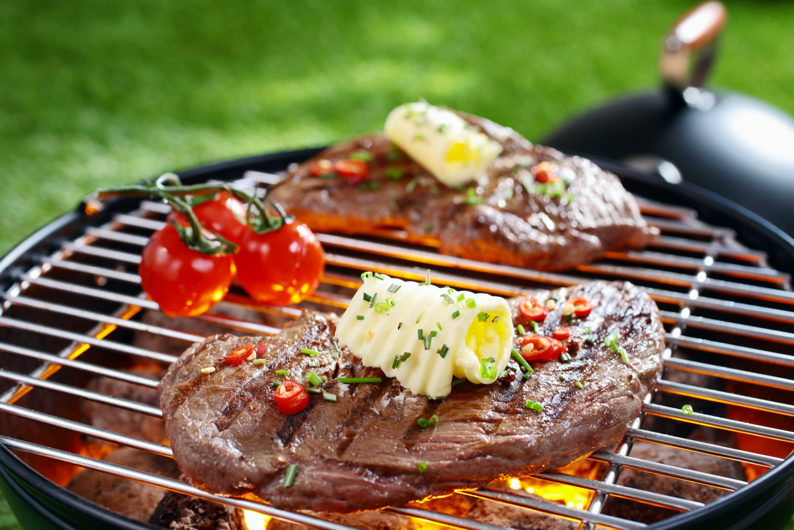 Succulent portion of lean steak topped with butter and herbs grilling on a grid over hot coals in a barbecue