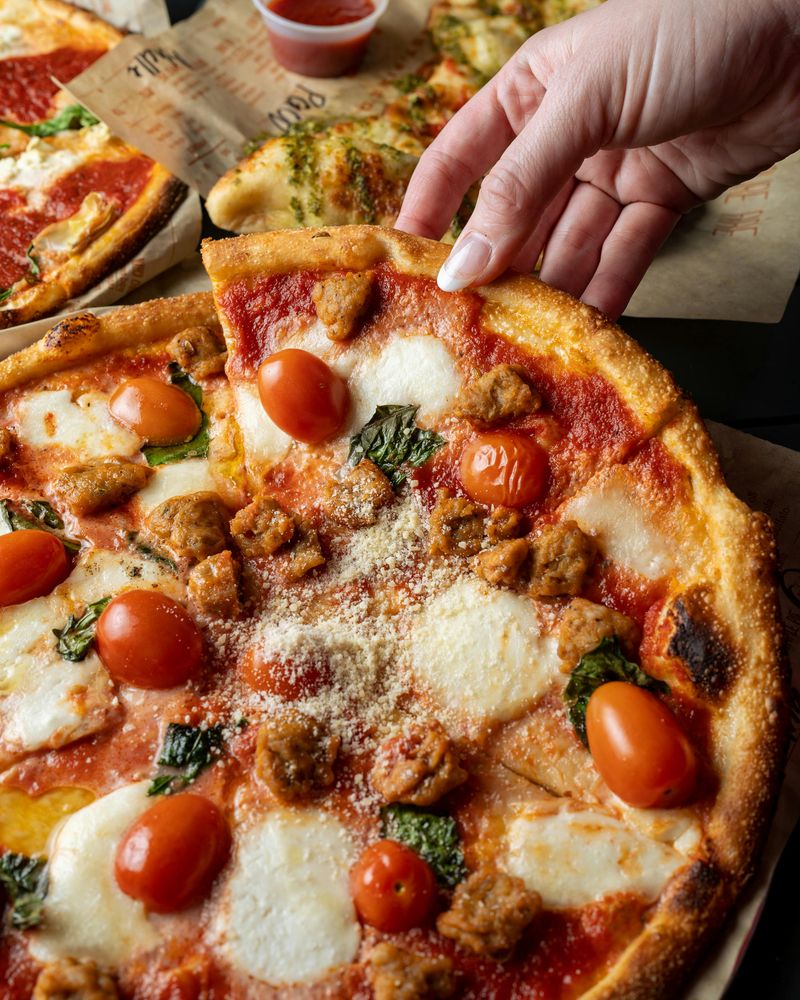 A Person Holding a Sliced Pizza with Tomatoes and Cheese