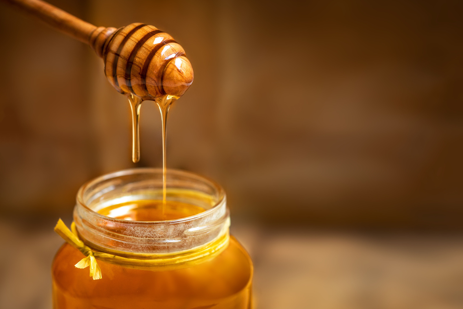 Honey in a glass jar with honey dipper on rustic wooden table background. Copy space. 
