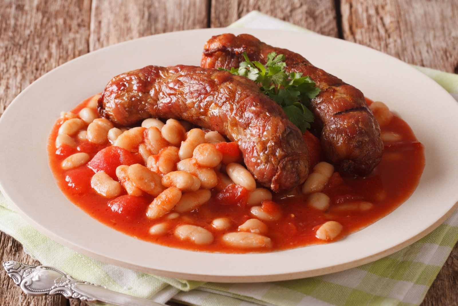 Pork sausages with beans and cooked tomatoes on a plate close-up on the table. Horizontal