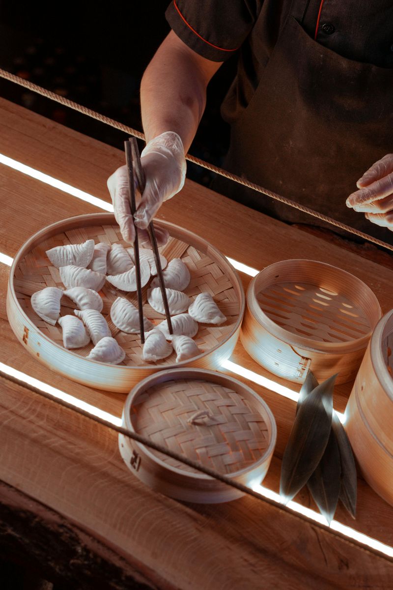 Person Preparing Dumplings Using Chopsticks on Bamboo Steamer