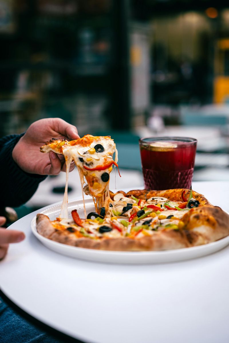 Hand Holding Pizza Slice with Beverage on Table