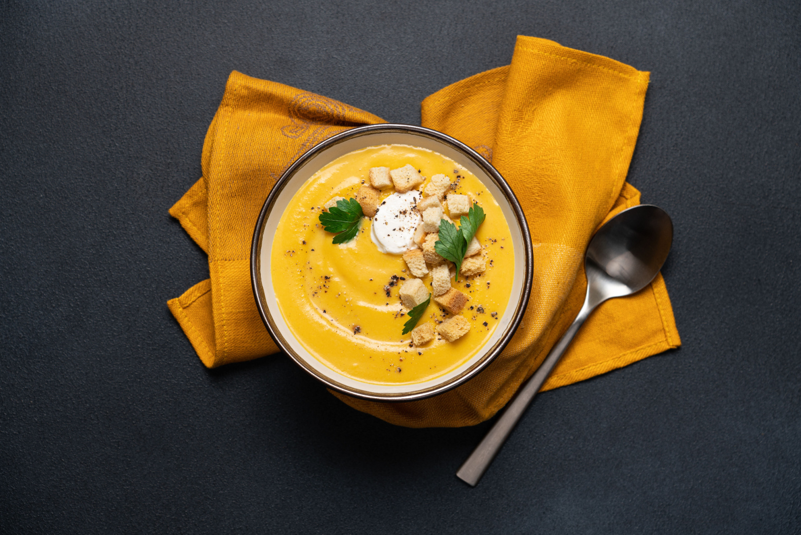 Pumpkin soup with cream and bread croutons in bowl on black background. Seasonal autumn dish on the table top view