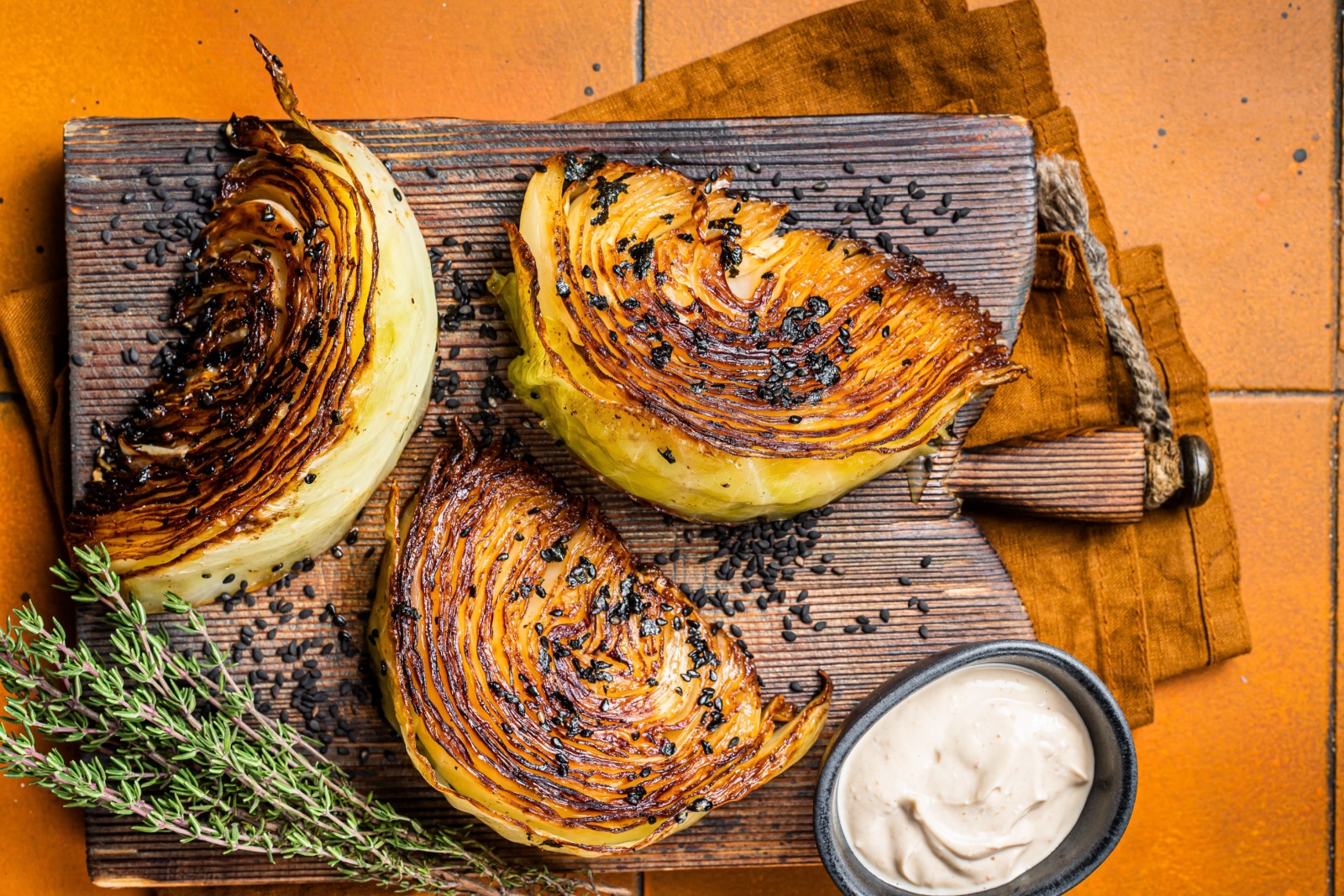 Roasted vegan cabbage steaks with herbs on wooden board. Orange background. Top view.