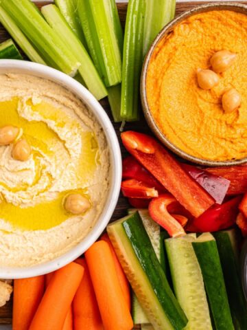 Various hummus dips. Hummus plate with vegetable snacks. Carrot, cucumber, tomato, celery sticks, dry crackers and olive, top view. Vegan and traditional hummus as healthy and vegan snack.