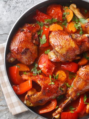 Homemade rooster stew with bell peppers, onions and carrots in a spicy tomato sauce close-up in a pan on the table. Horizontal top view from above