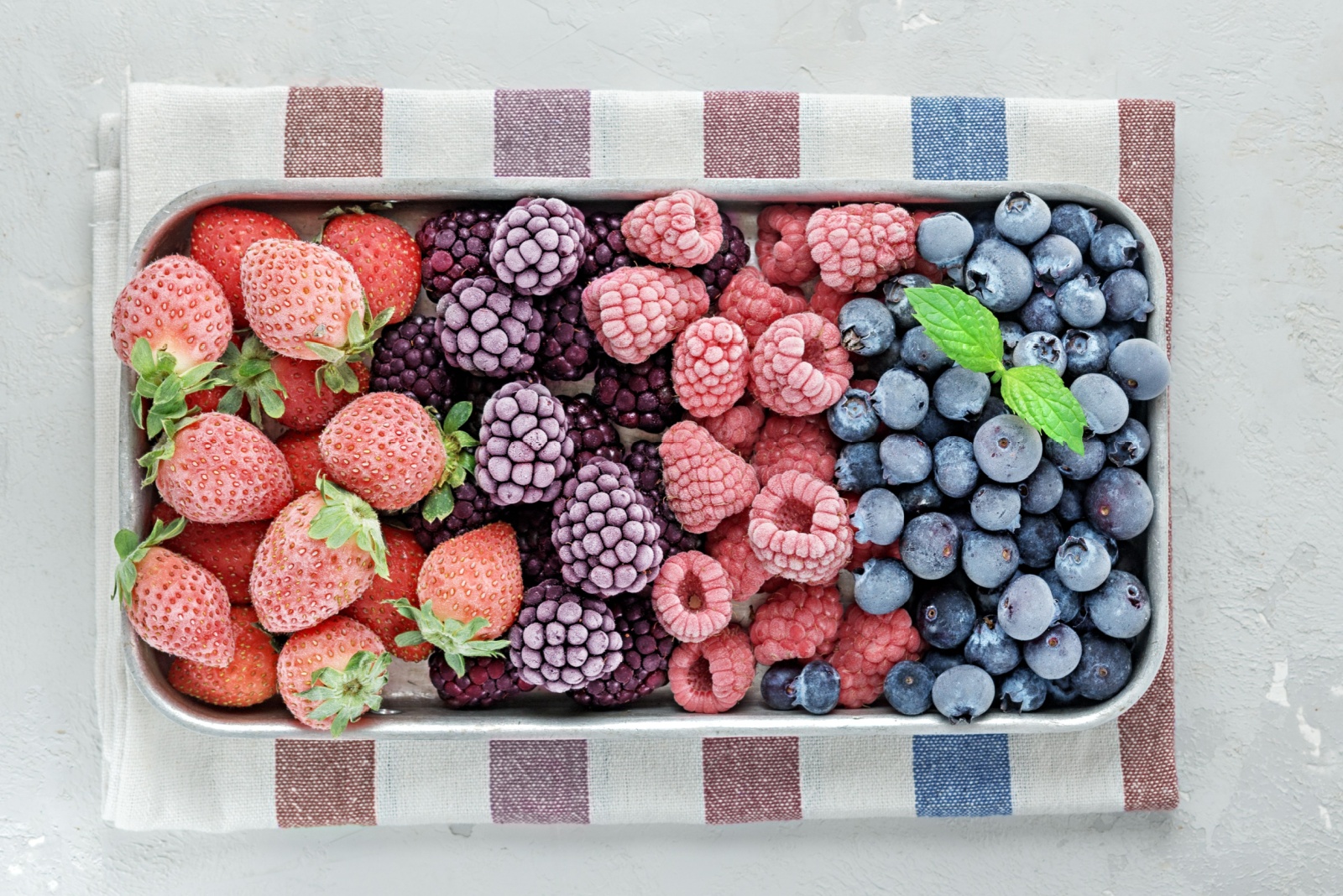Frozen berries in a metal tray on grey concrete.