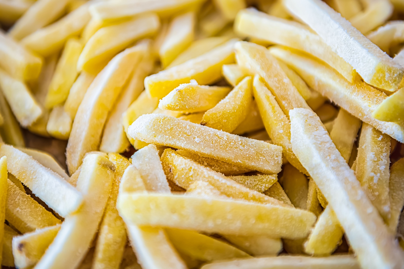 Macro closeup of frozen uncooked raw straight cut salty french fries pommes frites on oven baking tray before cooking or frying with texture detail