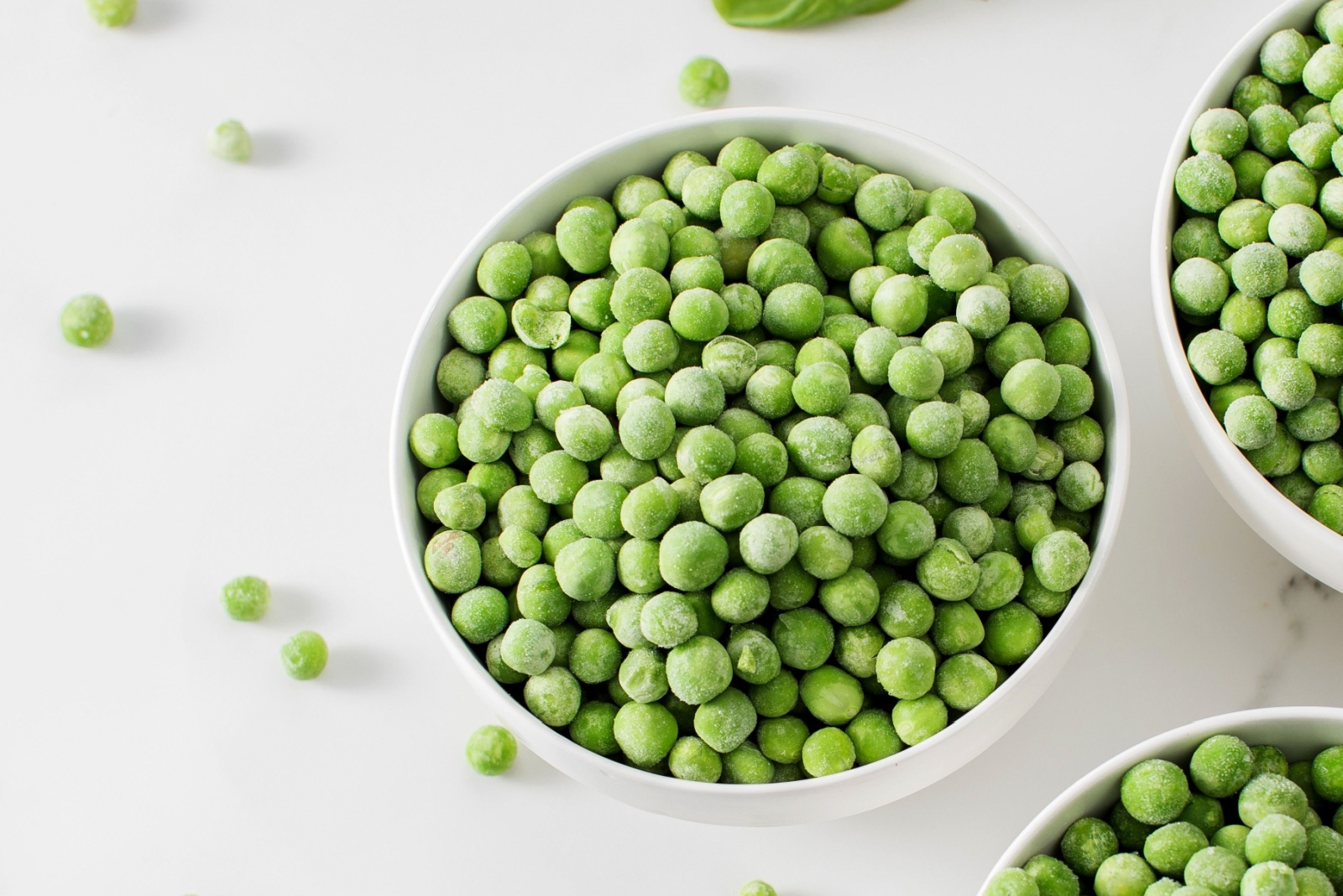 Three bowls of frozen green peas on a marble surface. Healthy vegetables