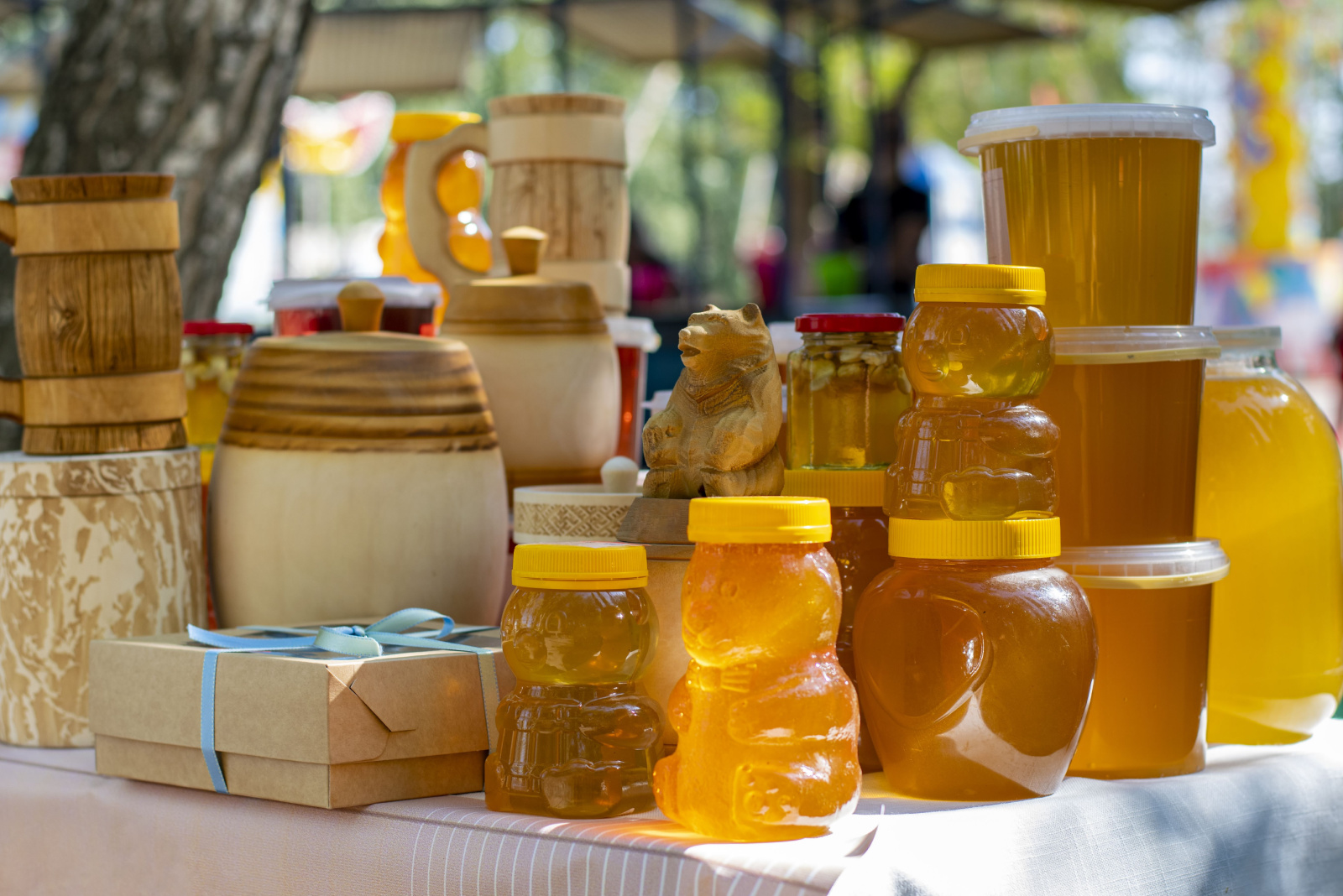 On the table are glass jars, wooden barrels and plastic containers filled with bee honey and ready to be sold at the honey fair 