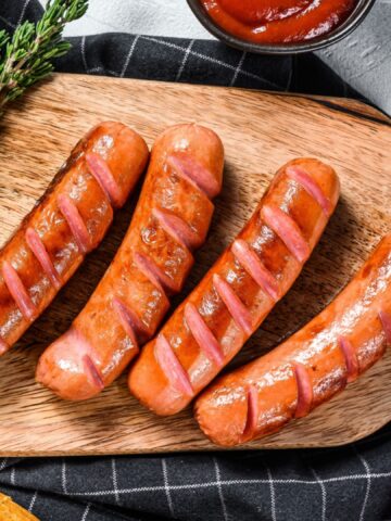 Ingredients for making homemade hot dogs. Sausages, fresh baked buns, mustard, ketchup, cucumbers. White background. Top view