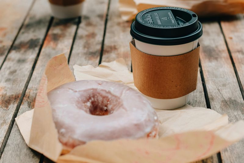 Delicious donut and takeaway coffee placed on wooden surface