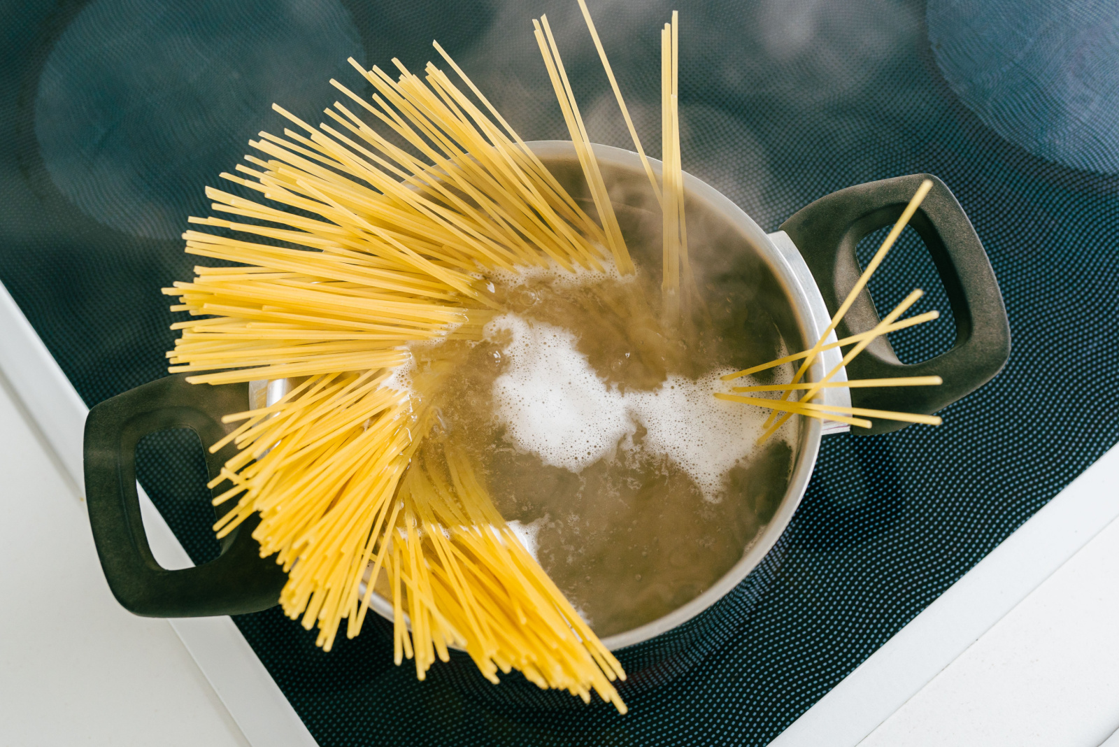 Spaghetti in pot is cooked in boiling water on electric ceramic hob. Top view, soft focus, yellow gluten free corn pasta cooking bolognese. Spaghetti in boiling steaming water