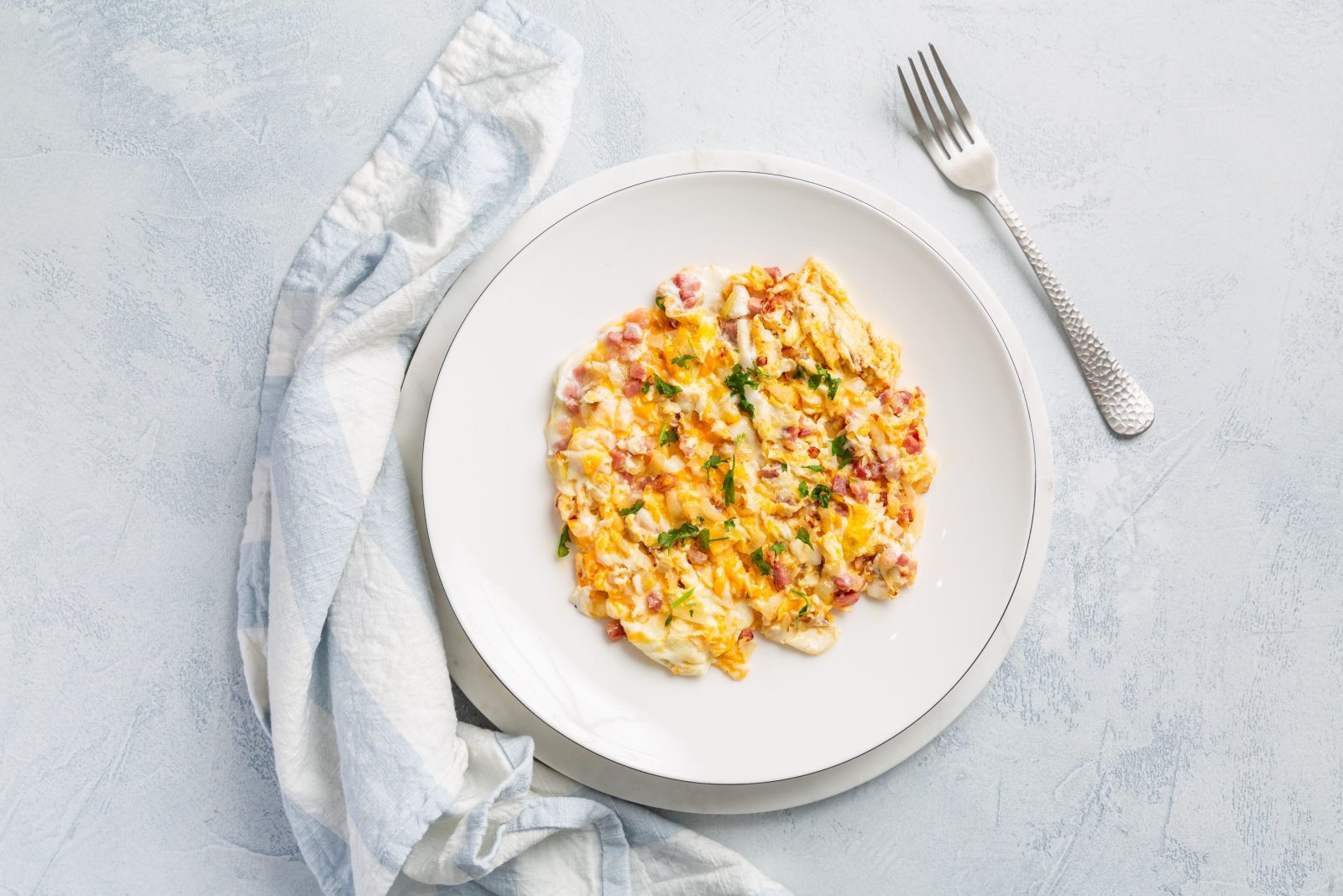 Homemade scrambled eggs with onions, bacon and herbs on white kitchen table