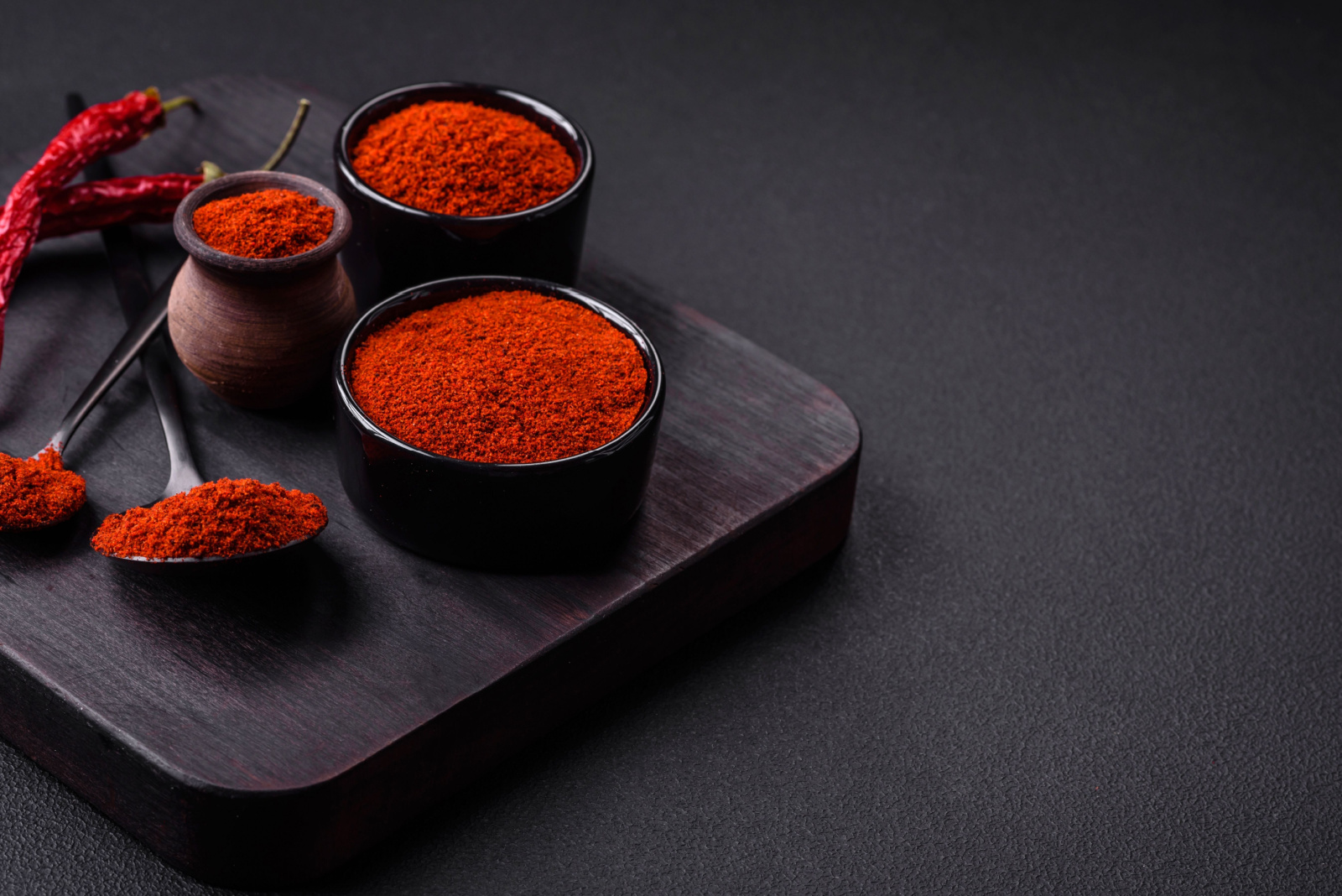 Spice smoked paprika in the form of powder in bowls and spoons on a dark concrete background. Asian cuisine ingredients