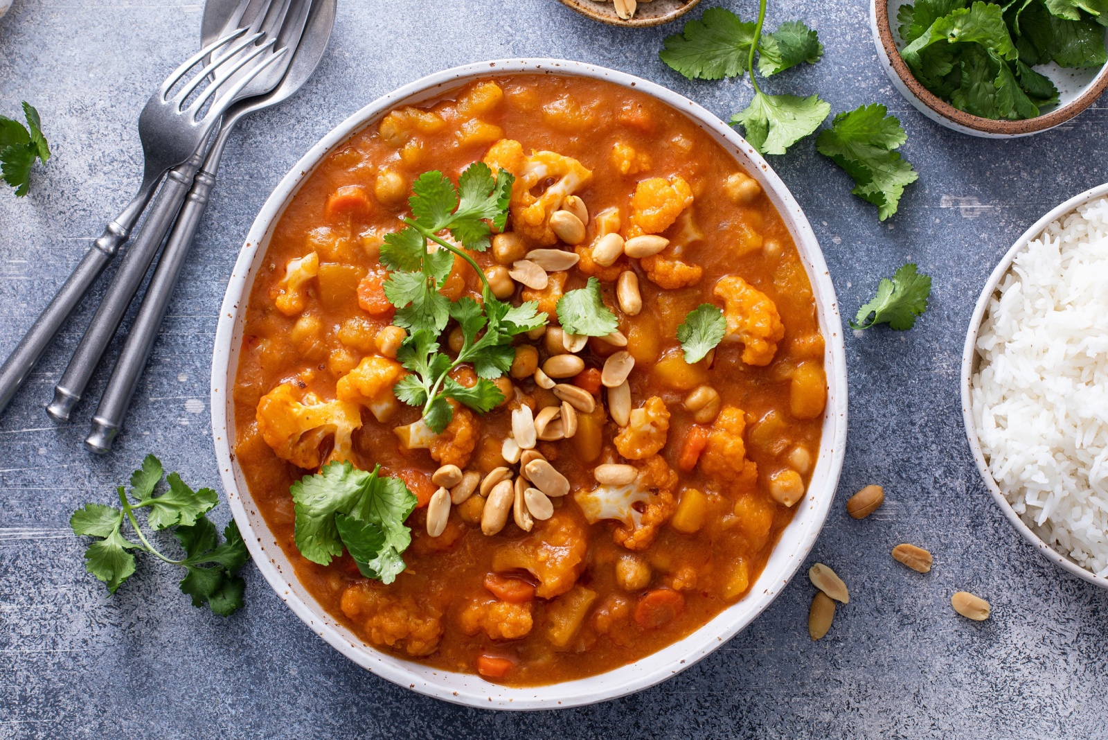 Vegan curry with cauliflower, chickpeas and butternut squash topped with peanuts, served with rice and cilantro