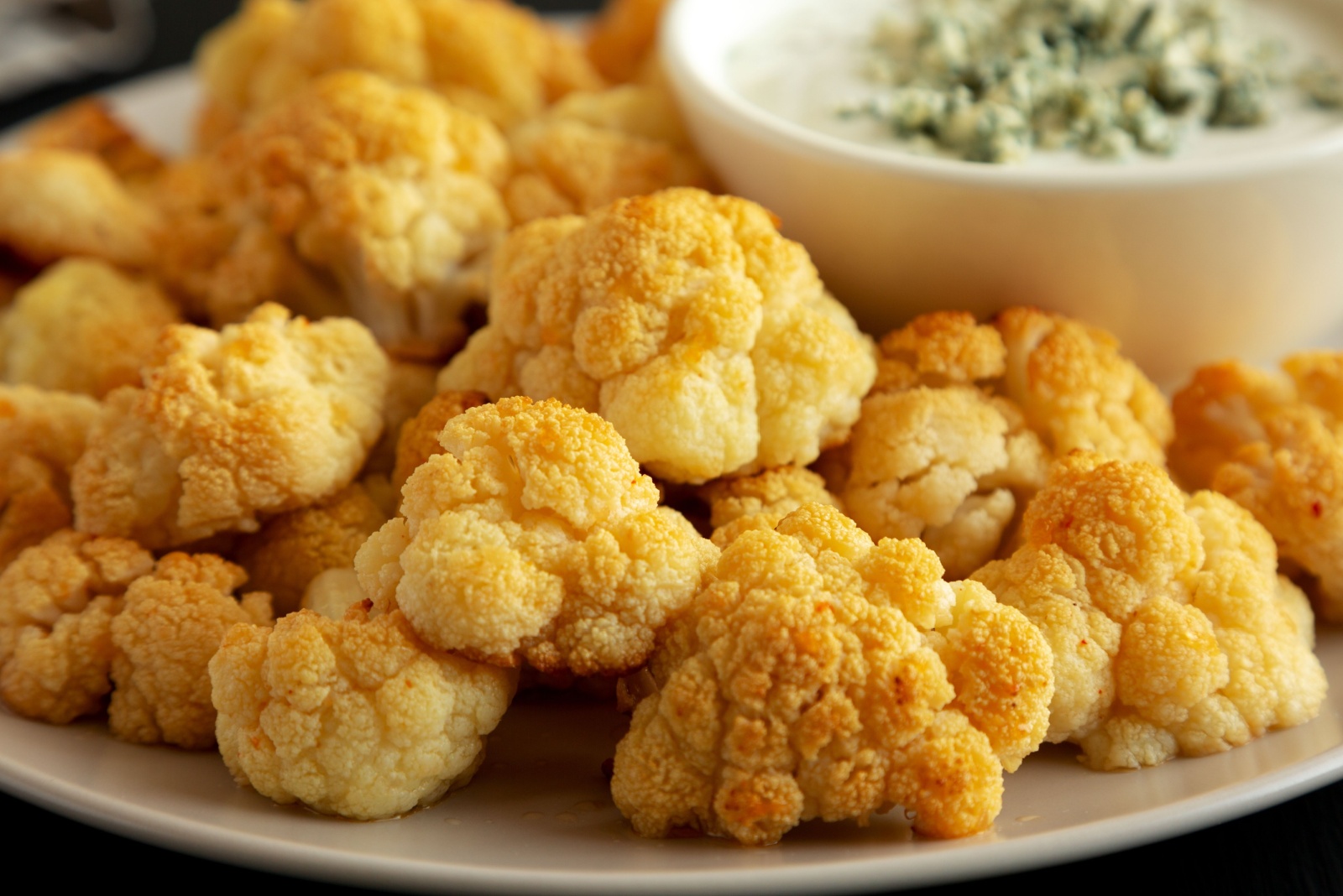 Homemade Buffalo Cauliflower with Blue Cheese Sauce on a Plate on a Black Background, side view. Close-up.