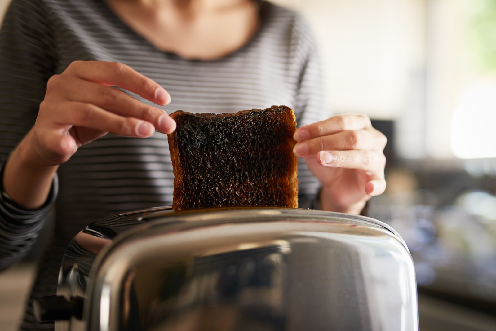 Hands, woman and burnt toast for breakfast in kitchen as cooking disaster, fail and accident as mistake in morning. Frustrated, person and black bread for unhealthy, electrical problem or safety